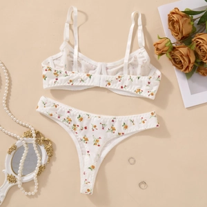 Flat lay detail of a floral lace bra set with pearl necklace and vintage mirror