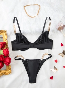 Détail d'un ensemble de lingerie en satin noir avec chaînes dorées sur fourrure blanche
