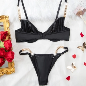 Ensemble lingerie satin noir avec chaînes dorées et string sur fond de fourrure blanche