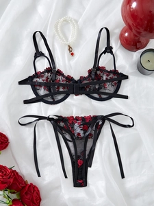 Flat lay of black floral lace lingerie set with red rose embroidery and ribbon bows