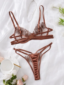 Flat lay of bronze embroidery lace bra and thong set with silk and rose accents