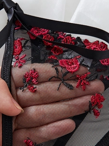 Detailed close-up of sheer black mesh lingerie featuring vibrant red floral embroidery