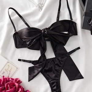 Close-up of black satin lingerie set with large bow detail and pearl accessories