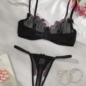 Flat lay of black sheer mesh lingerie set with pink floral embroidery on white plush carpet