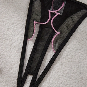 Detail of black mesh thong with pink embroidered feminine silhouette on white fur