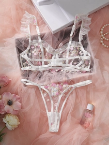 Detailed close-up of white mesh bra set with floral embroidery on pink decorative background