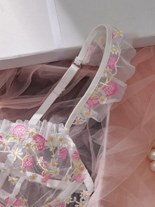 Detail of white mesh bra featuring strawberry embroidery and romantic ruffle trim
