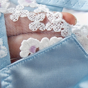 Macro detail of blue lingerie featuring white floral lace embroidery and transparent mesh fabric