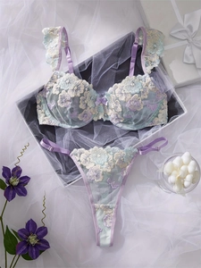 Macro view of lilac lace lingerie set with colorful floral embroidery on a white gift box