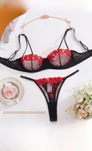 Dettaglio del set di lingerie in rete nera con ricami floreali rossi e gruccia oro rosa