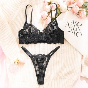 Flat lay of black floral lace lingerie set with roses and vintage perfume bottle
