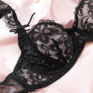 Close-up of black floral lace bra with underwire and eyelash trim on pink silk