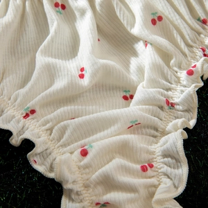 Détail du tissu en maille côtelée crème avec imprimé cerise et bords volantés délicats