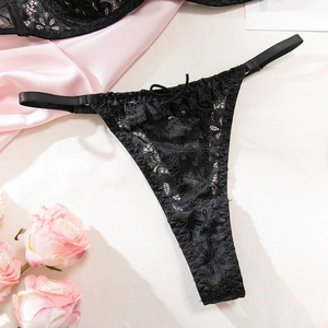 Close-up of black floral lace G-string panty with delicate bow on satin background