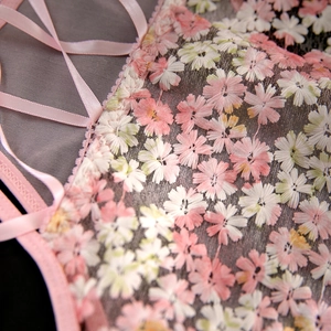 Macro detail of pink floral embroidery and satin lace-up ties on sheer mesh fabric
