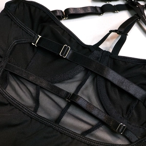 Detail of black mesh bodysuit with adjustable straps and metal buckles on white background