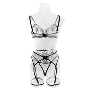 Detailed view of white floral lace lingerie set with black satin trim on a clear mannequin