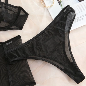 Flat lay of black sheer mesh lingerie set with accessories on light pink tulle background