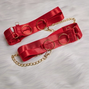 Détail de jarretières en satin rouge avec anneaux métalliques dorés et chaînes fines