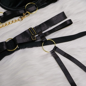 Détail d'un harnais noir avec anneaux et chaînes en métal doré sur fausse fourrure blanche