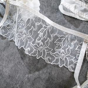 Macro detail of white floral lace embroidery with sparkling crystal chain shoulder straps