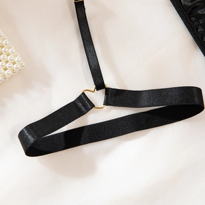 Detail of black elastic straps with gold heart-shaped metal rings and pearl accent