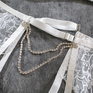 Detailed macro view of white lace embroidery with crystal chains and silver buckle