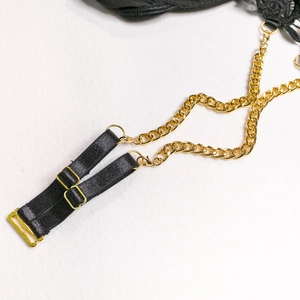 Detailed close-up of black lace lingerie with gold metal chain straps and adjustable hooks