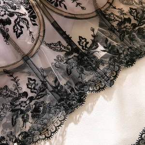Detailed macro view of black floral embroidery and lace on a white satin corset top