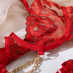 Detail of red flame embroidery on mesh bodysuit with golden metal chain accents