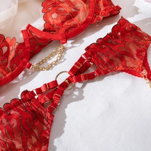 Close-up of red lace lingerie featuring detailed flame embroidery and gold chain metal accents