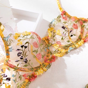 Détail d'un soutien-gorge en maille jaune avec broderies florales colorées et dentelle festonnée