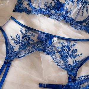 Macro view of blue floral embroidery and satin bow detail on a white lace bodysuit