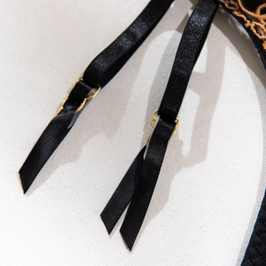 Detail of black adjustable shoulder strap with gold metal buckle and floral embroidery