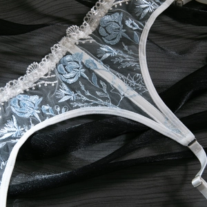 Detailed close-up of white lace bra with light blue floral embroidery and satin edges