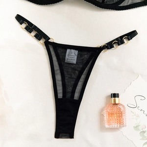 Detail view of black mesh thong with gold metal rings and sizing label on fabric background