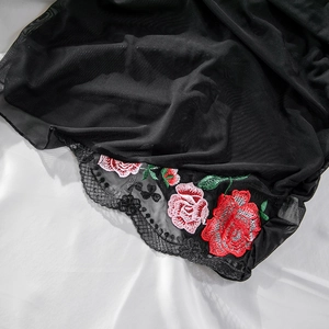 Detailed macro view of delicate rose floral embroidery on black mesh and lace fabric