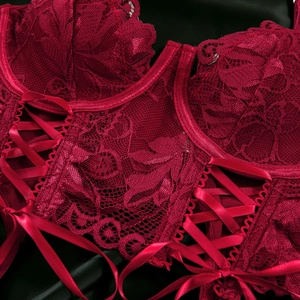 Detailed close-up of dark red floral lace corset with satin criss-cross ribbon lacing
