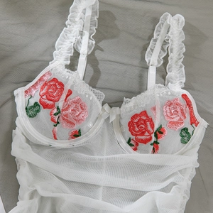 Detail of white lace bodysuit with pink rose floral embroidery and ruffled straps