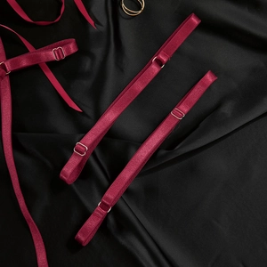 Macro detail of maroon adjustable elastic lingerie straps with metal buckles on black silk