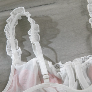 Detail of adjustable shoulder strap with lace ruffles and metal buckle on white bodysuit