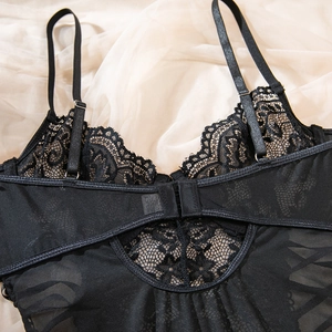 Close-up of black eyelash lace bodysuit with adjustable straps on beige silk fabric