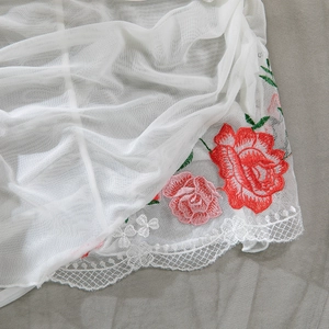 Detailed view of floral embroidery and scalloped lace trim on white mesh lingerie fabric