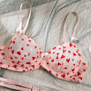 Détail d'un body en tulle rose avec motifs cœurs rouges, armatures et petits nœuds