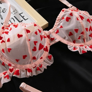 Détail du soutien-gorge en maille rose avec cœurs floqués rouges et bordure plissée
