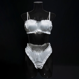 Detail of white satin lingerie set with pleated edges and adjustable straps on black background