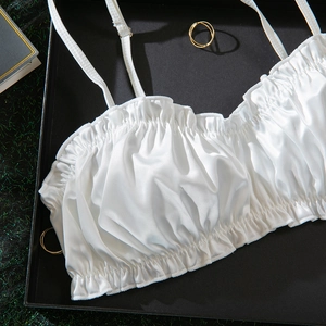 Detailed view of white ruched satin camisole top with ruffled edges in a flat lay setting