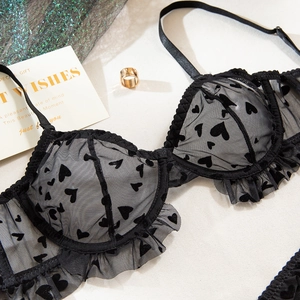 Détail d'un soutien-gorge en maille noire avec motifs cœurs floqués et bords plissés