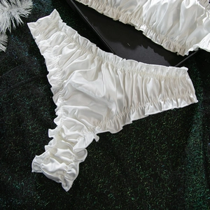 Detail of white satin lingerie panties with pleated edges and silky texture on a dark base