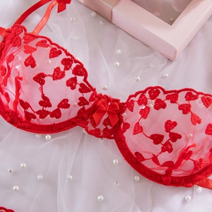 Dettaglio del reggiseno in pizzo rosso con ricamo a cuore, fiocco e tessuto trasparente